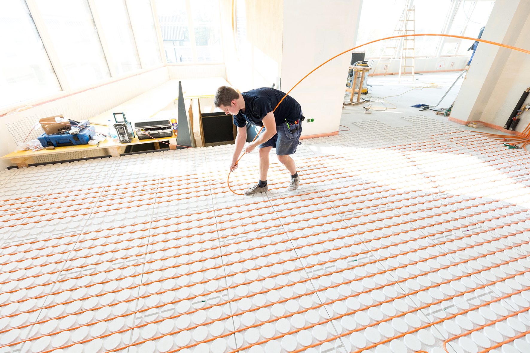 Installateur legt de verwarmingsbuis in de systeemplaten van een droogbouwvloer