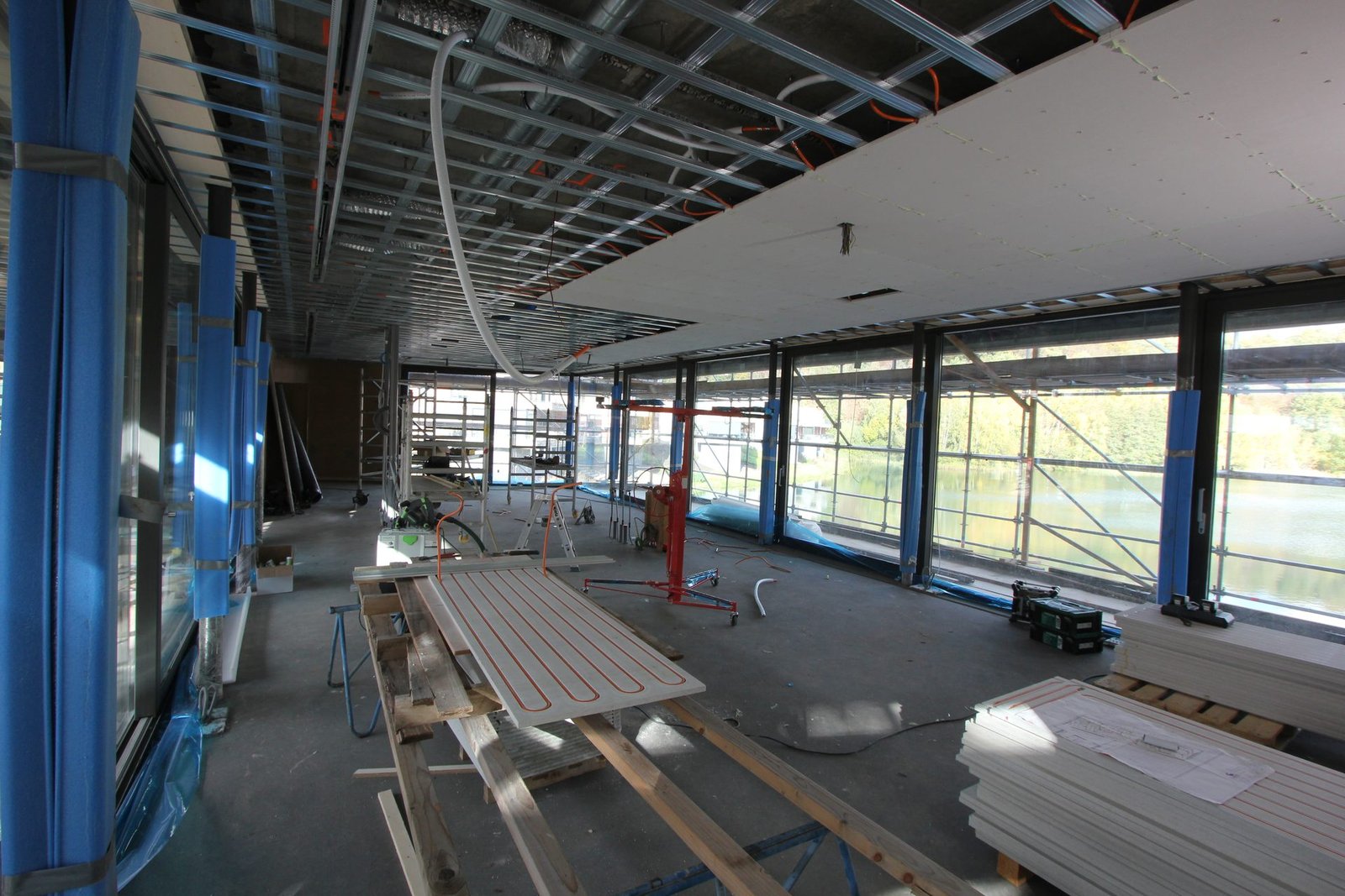 Woonruimte in aanbouw met regelwerk aan het plafond en stapels klimaatplafondplaten op de vloer