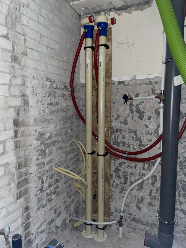 Twee verticale douchepijp-wtw's tegen een gemetselde muur, aangesloten op de afvoer en de waterleiding