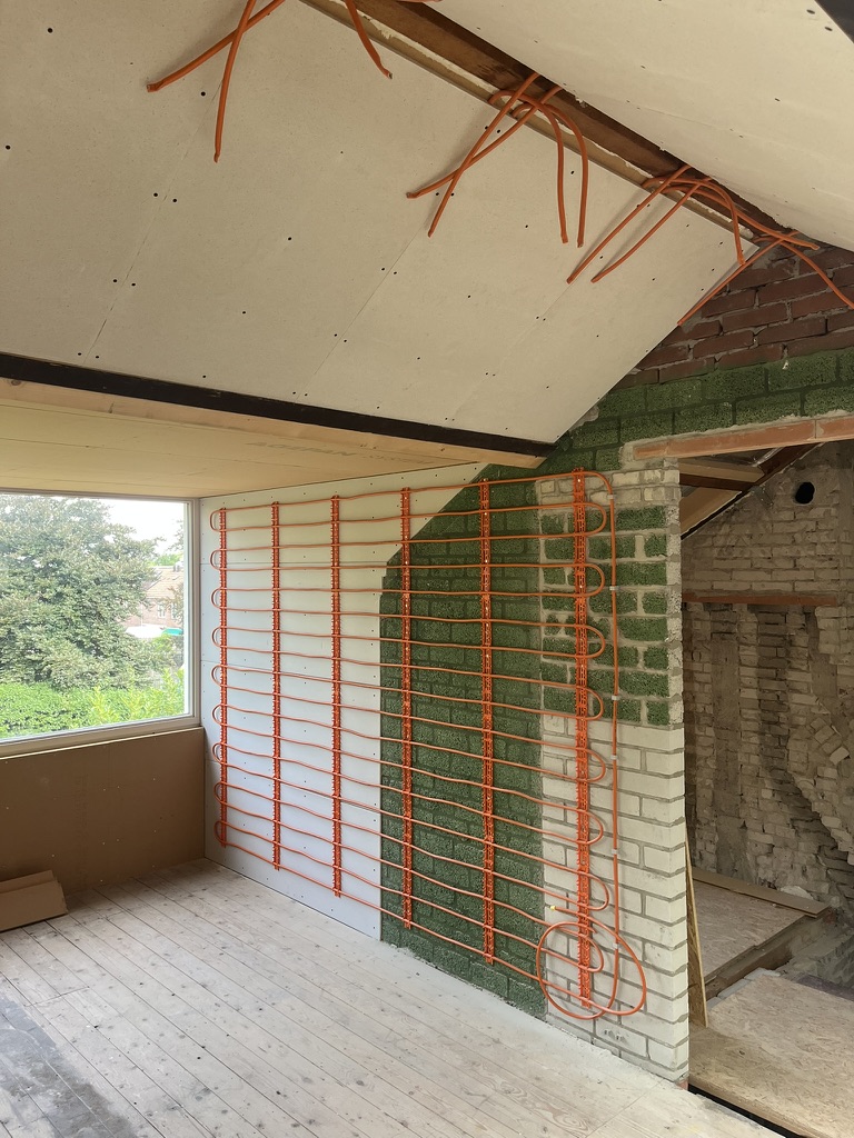 Zolderkamer met oranje Varioprofielbuis op de wanden: links op isolatieplaten, rechts op de gemetselde muur